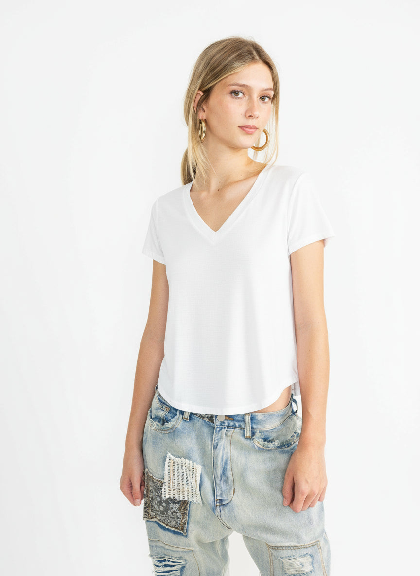 Woman wearing a white V-neck t-shirt and light blue jeans with patches on a white background