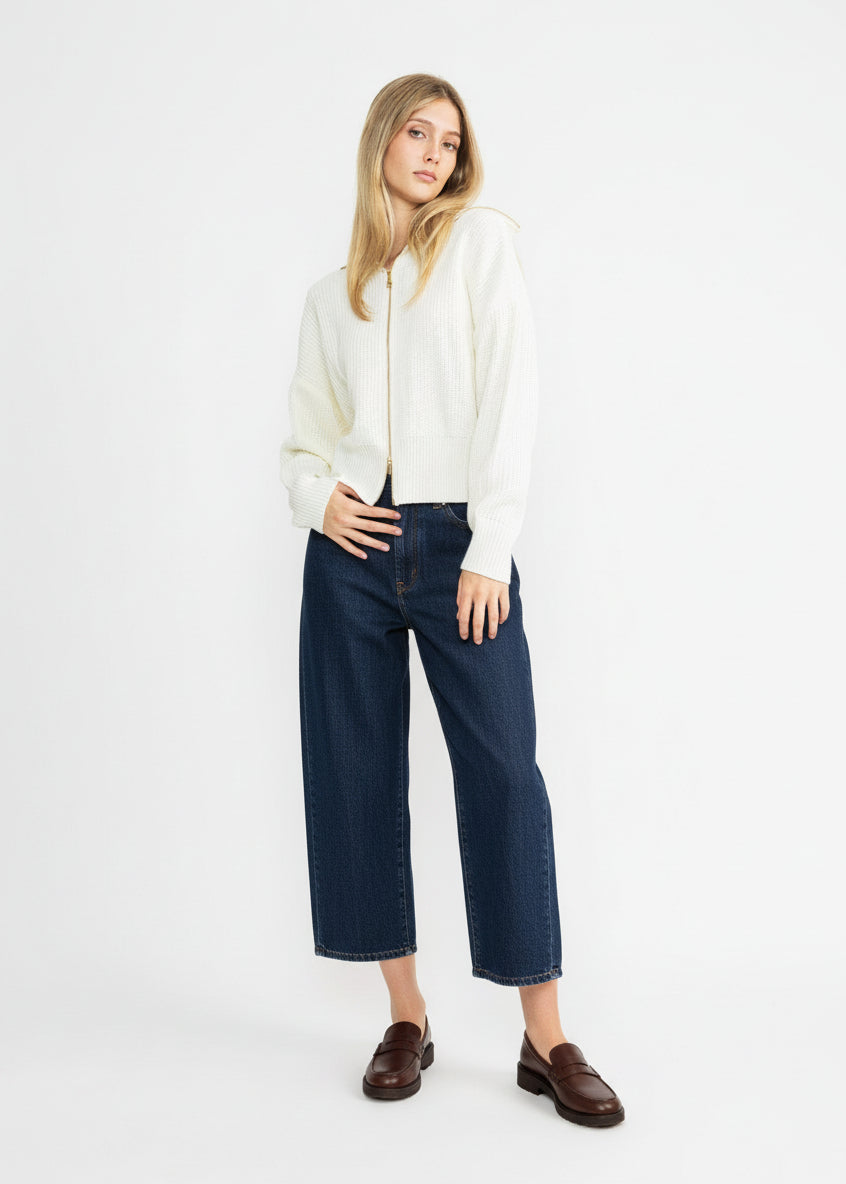 Woman wearing a white sweater, dark blue jeans, and brown shoes on a white background