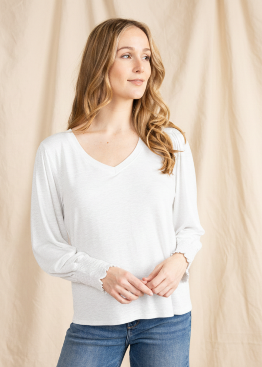 Woman wearing a white tee and blue jeans against a beige curtain background