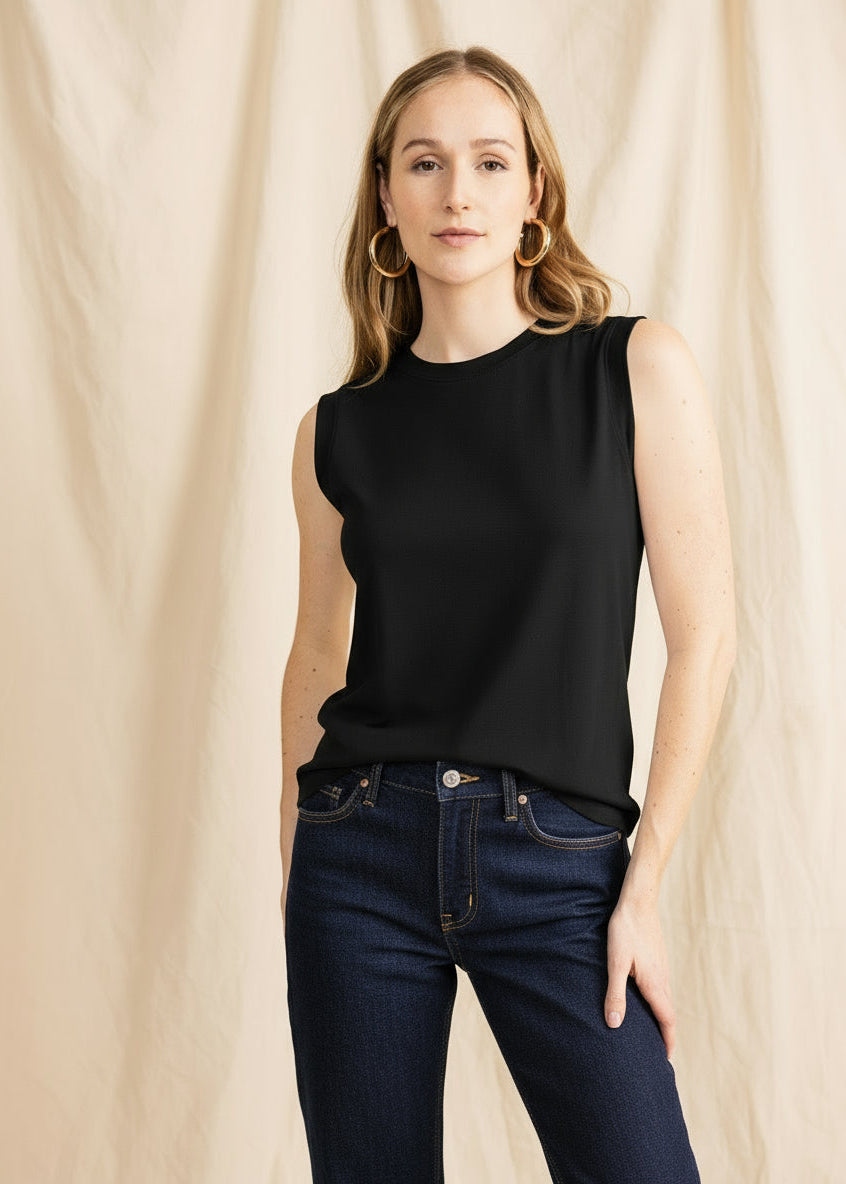 Woman wearing a white sleeveless top and blue jeans against a beige background