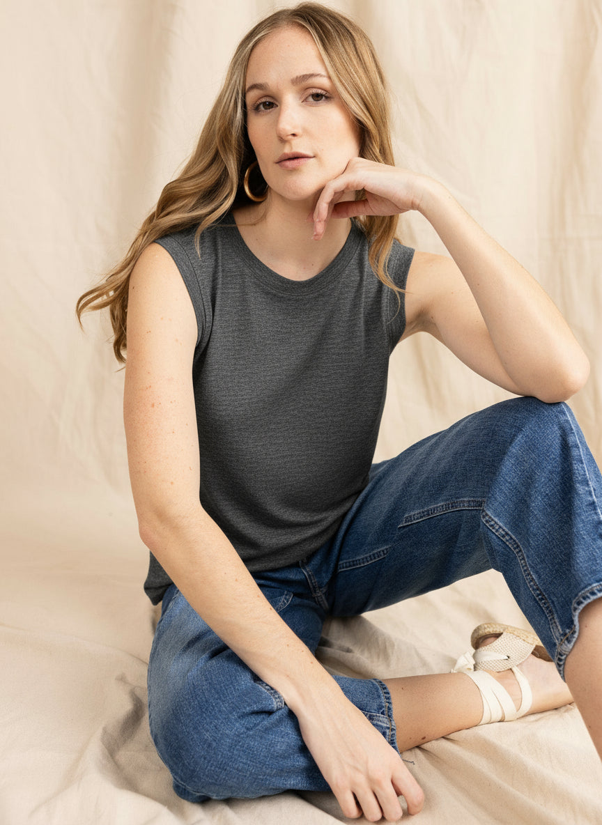 Woman wearing a white sleeveless top and blue jeans sitting on a beige surface.