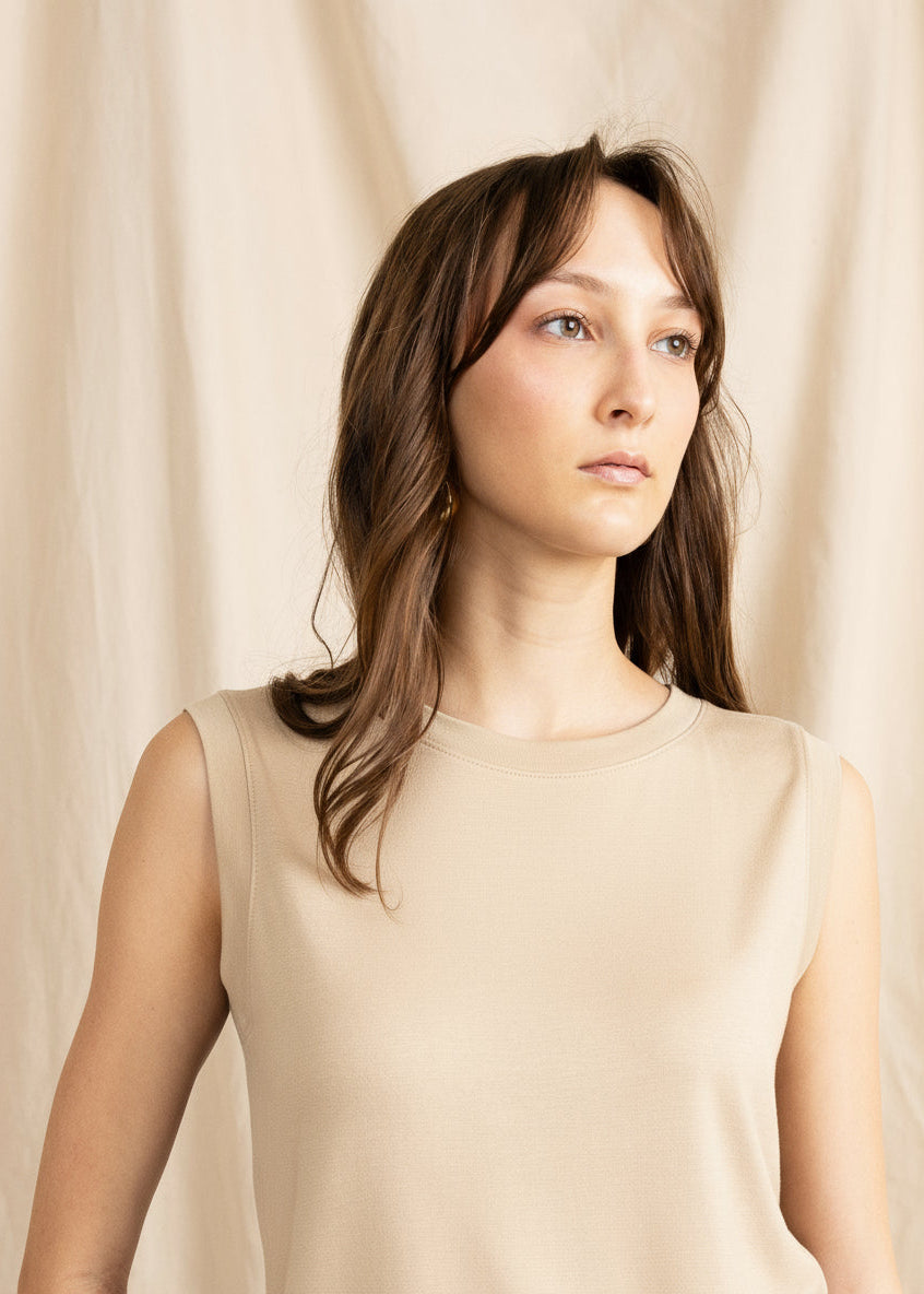 Woman wearing a beige sleeveless top against a plain background