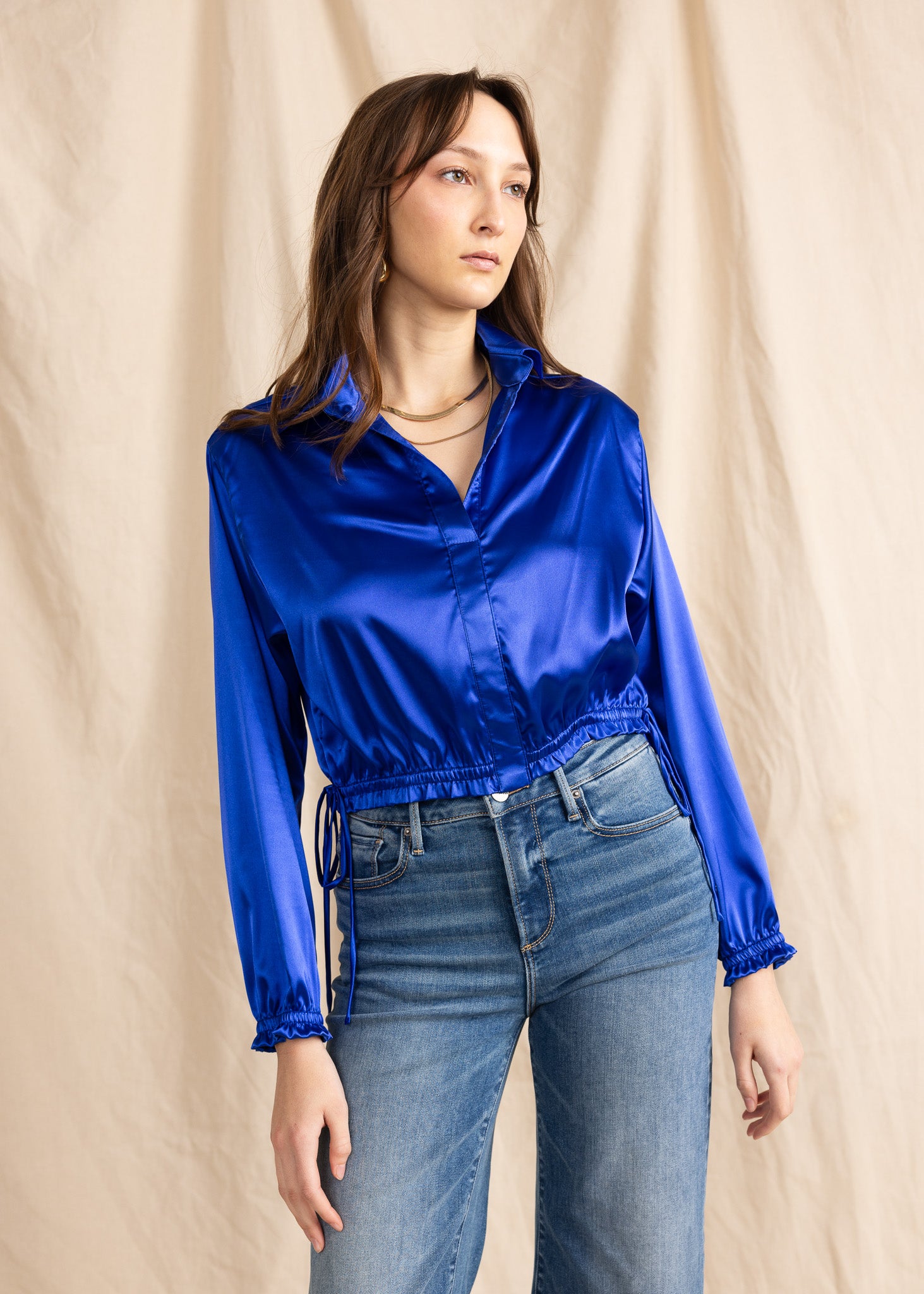 A person wearing a blue satin button-down top with ruffled cuffs and a collared neck, paired with blue jeans.