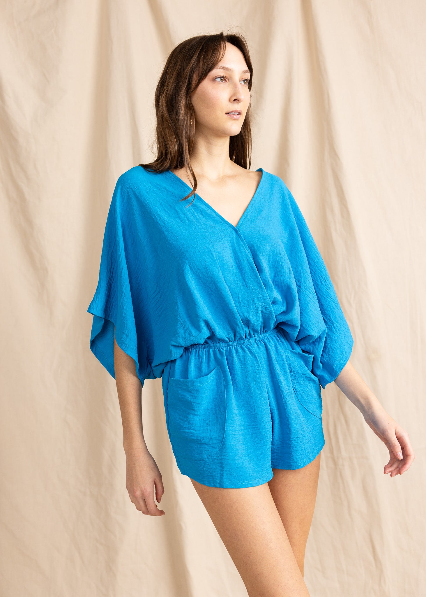 Woman wearing a blue romper against a beige background