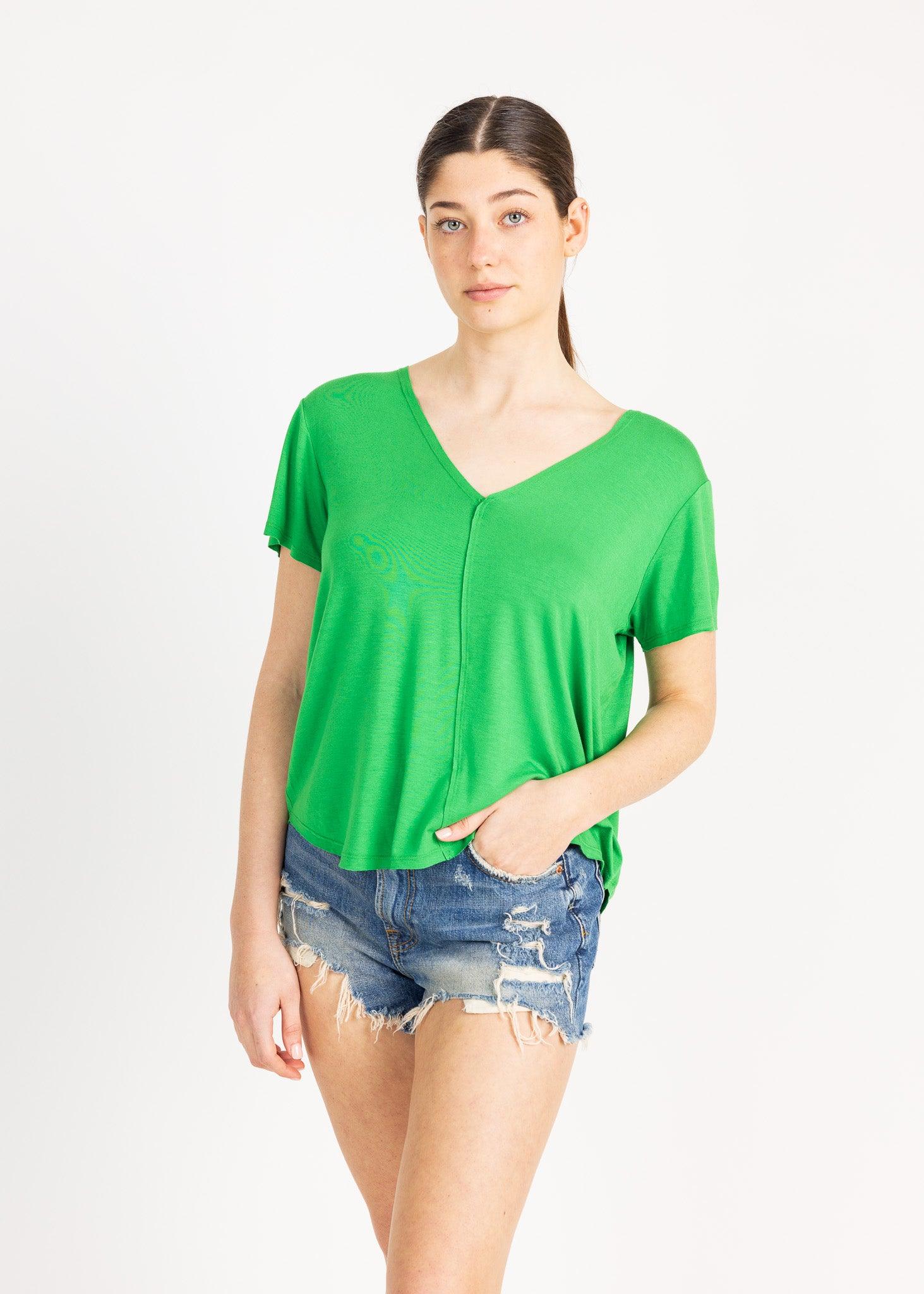 A woman wearing a green v-neck top and denim shorts, standing against a white background.
