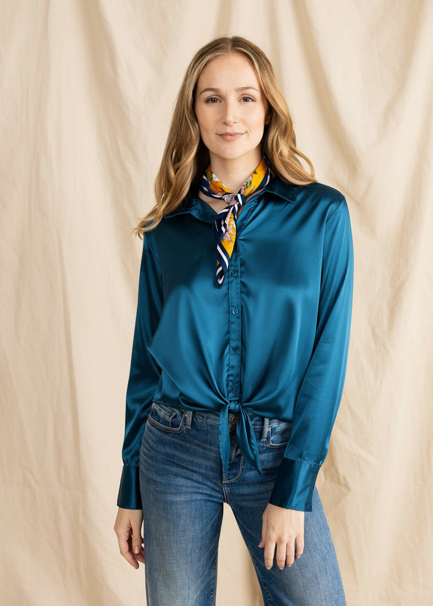 A woman wearing a beige satin blouse with a collared button-down design, tied at the front, paired with blue jeans.