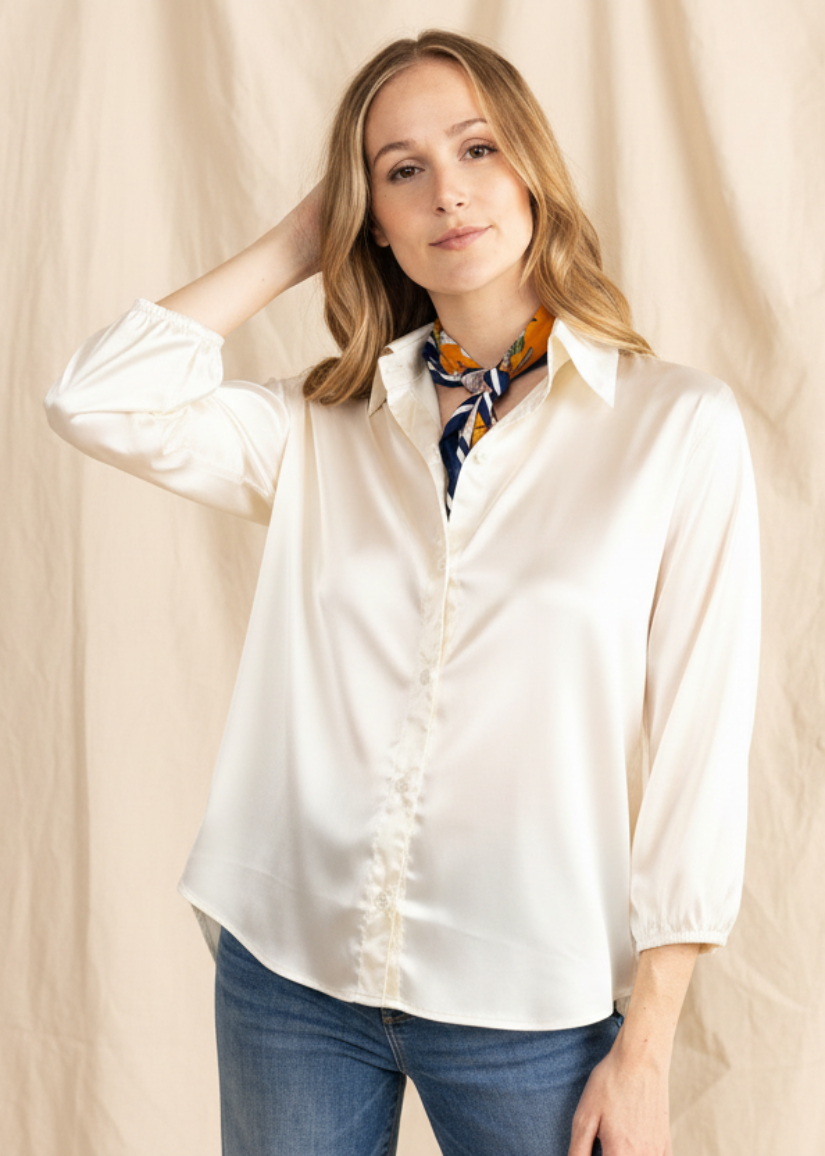 Woman wearing a white blouse and blue jeans with a colorful scarf, standing against a beige background