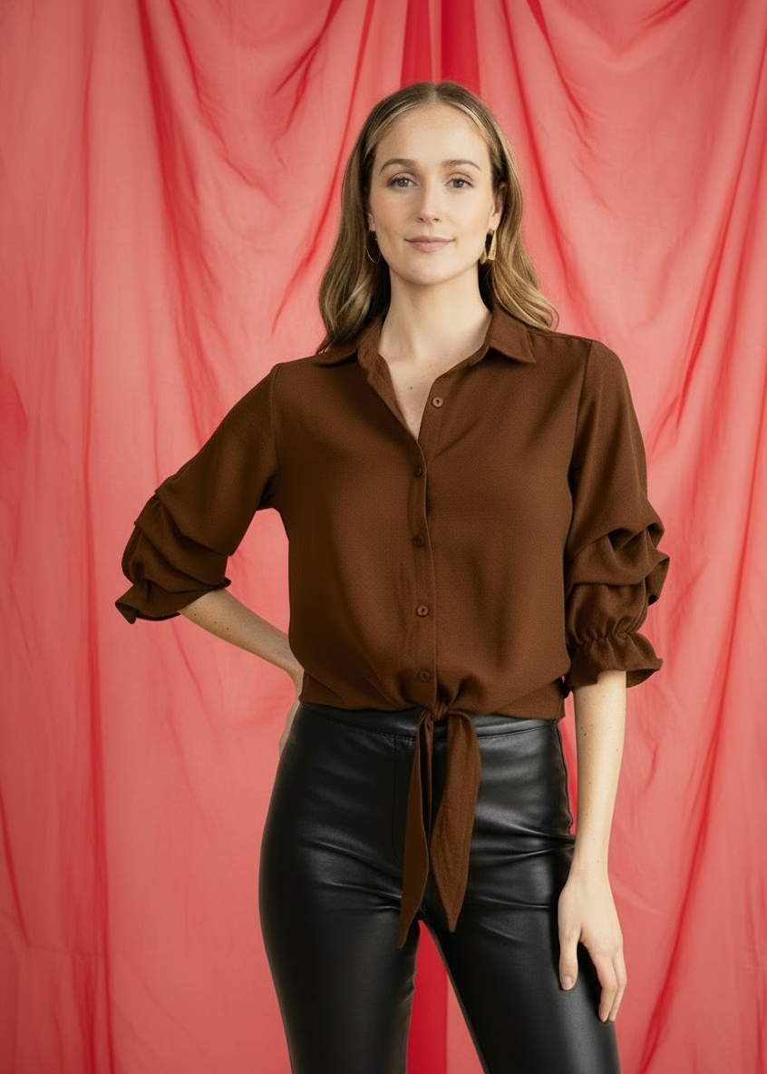 Woman wearing a brown blouse and black leather pants against a red curtain background