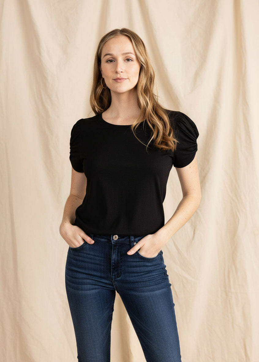Woman wearing a black top and blue jeans against a beige background