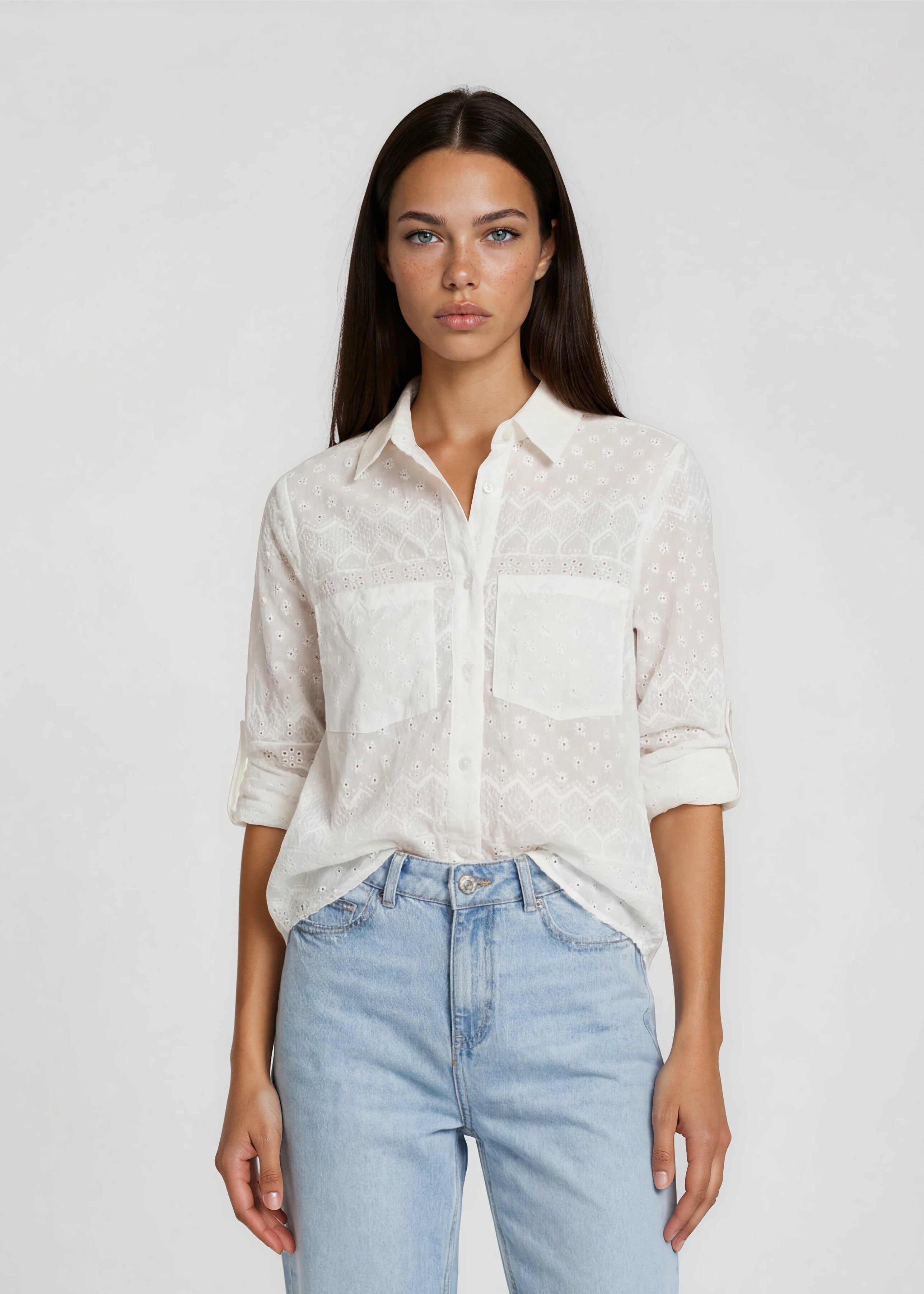 Woman wearing a white shirt and light blue jeans against a plain background