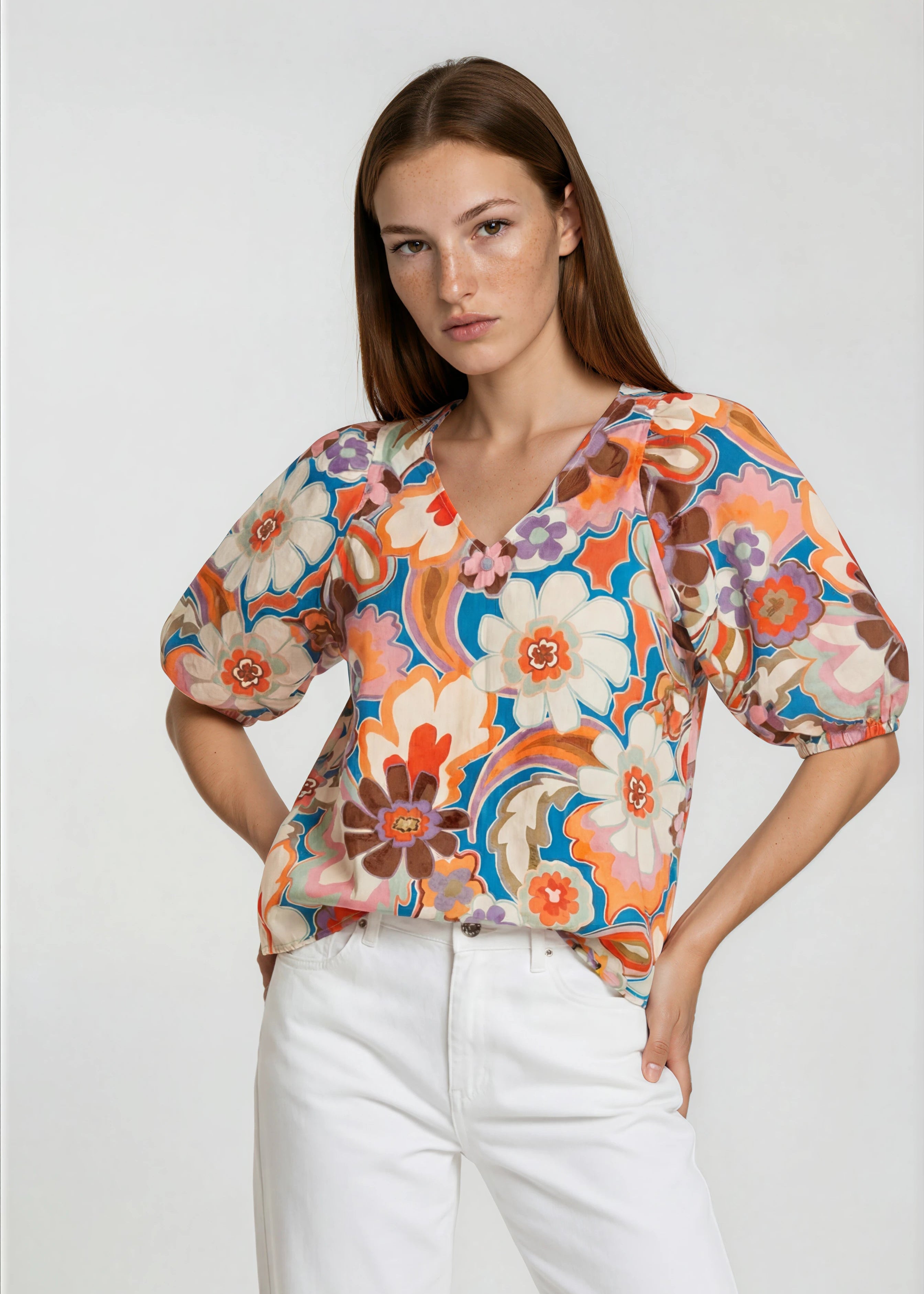 Woman wearing a colorful floral blouse with white pants on a plain background